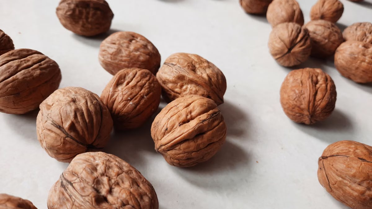 A detailed close-up of fresh whole walnuts scattered on a white background.
